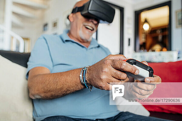 Fröhlicher älterer Mann  der einen Virtual-Reality-Simulator trägt und zu Hause ein Videospiel spielt