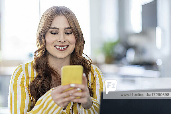 Lächelnde schöne Frau  die zu Hause ein Mobiltelefon benutzt