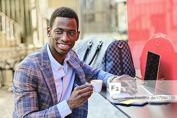 Smiling businessman with coffee cup sitting at sidewalk cafe