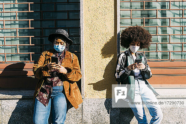 Multi-Ethik-Freunde mit Gesichtsschutzmaske bei der Nutzung eines Smartphones an einem sonnigen Tag