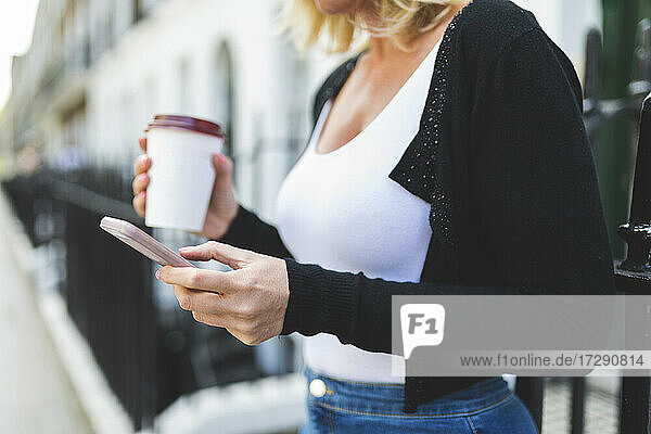 Frau mit Einweg-Kaffeebecher und Smartphone