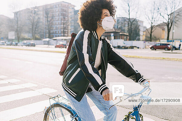 Frau mit Gesichtsmaske  die an einem sonnigen Tag Fahrrad fährt