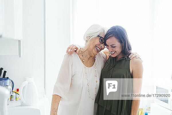 Fröhliche Großmutter und Enkelin stehen mit Arm in der Küche zu Hause