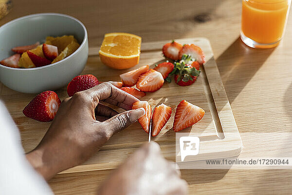Hände einer Frau beim Schneiden frischer Erdbeeren am Küchentisch