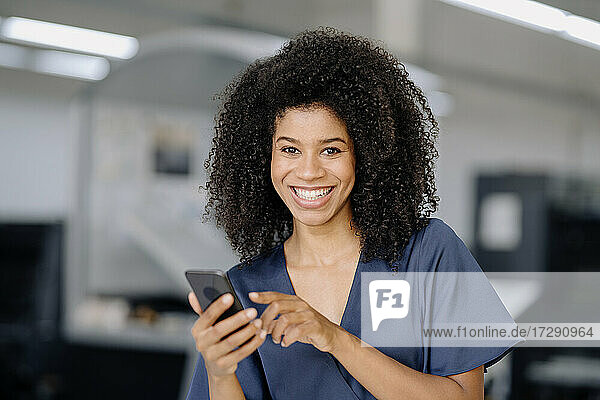Lächelnde Geschäftsfrau  die ein Smartphone hält  während sie im Büro steht