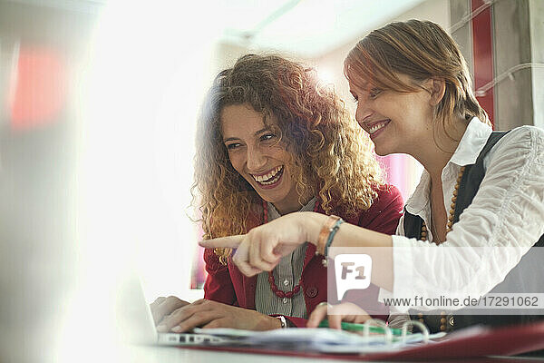 Fröhliche Freiberuflerinnen arbeiten an einem Laptop in einem Café
