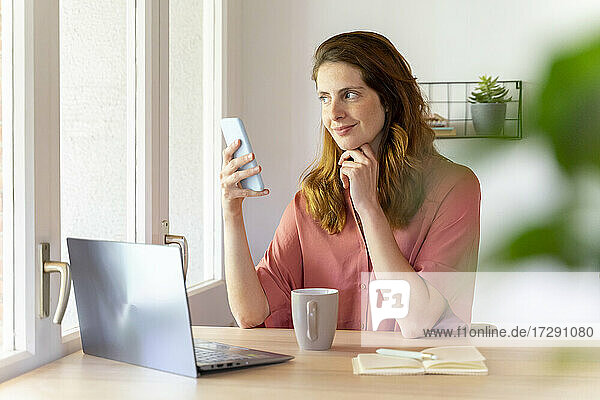 Weibliche Fachkraft schaut weg  während sie ein Smartphone im Büro zu Hause hält