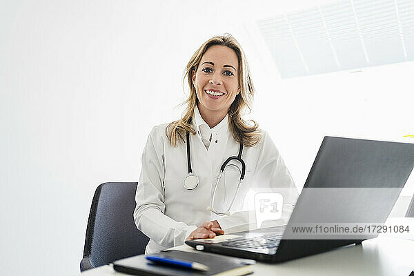 smiling female doctor with stethoscope sitting at desk in office