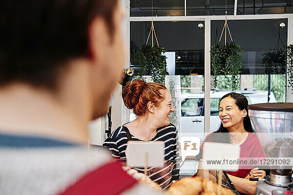 Lächelnde Kundinnen unterhalten sich am Tresen eines Cafés