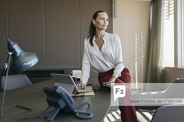 Berufstätige Frau mit Laptop und Mobiltelefon am Schreibtisch sitzend