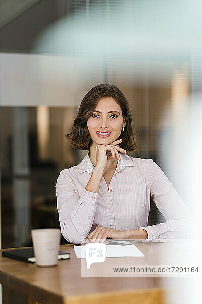 Beautiful young businesswoman sitting with hand on chin at desk in office