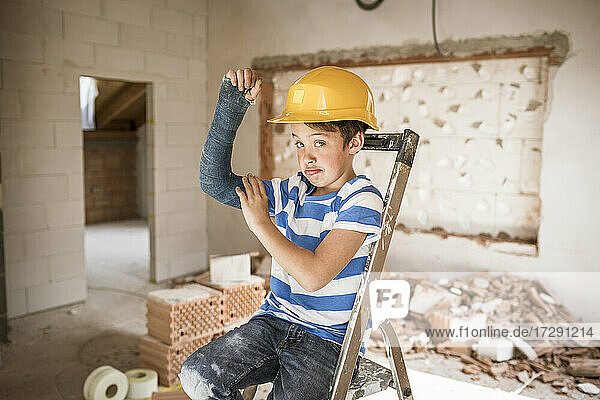Junge mit gebrochenen Armmuskeln  während er bei der Hausrenovierung auf der Leiter sitzt