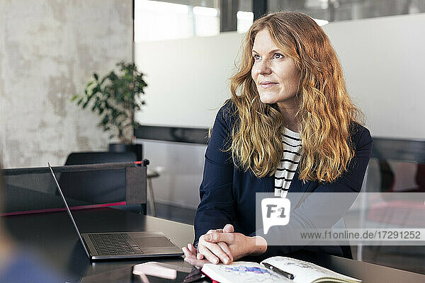 Geschäftsfrau mit braunen Haaren  die beim Sitzen im Büro wegschaut