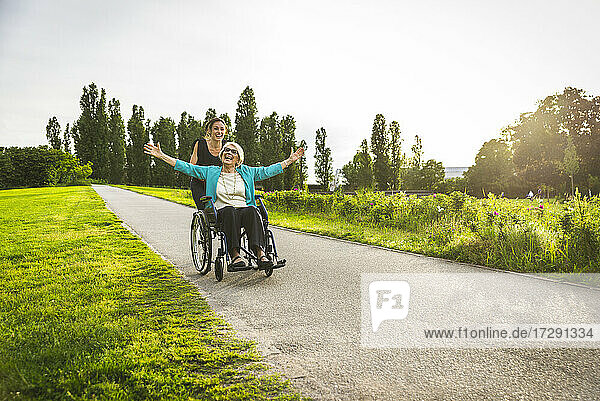 Fröhliche Enkelin spielt mit der im Rollstuhl sitzenden Großmutter im Park