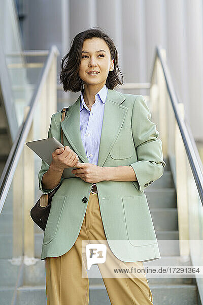 Selbstbewusste Geschäftsfrau  die mit einem digitalen Tablet im Büro steht und wegschaut