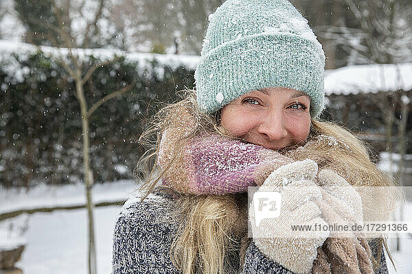 Blonde Frau bedeckt den Mund mit einem Schal  während sie bei Schnee im Hinterhof steht
