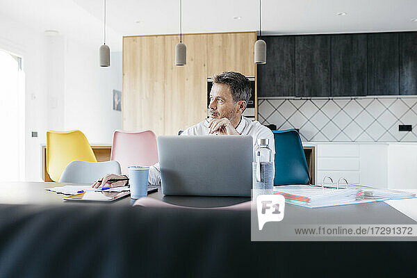 Male freelance worker contemplating while sitting at kitchen in home office