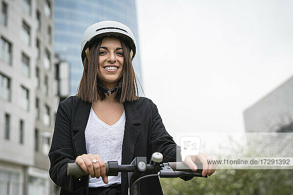 Businesswoman wearing cycling helmet smiling while standing with electric push scooter