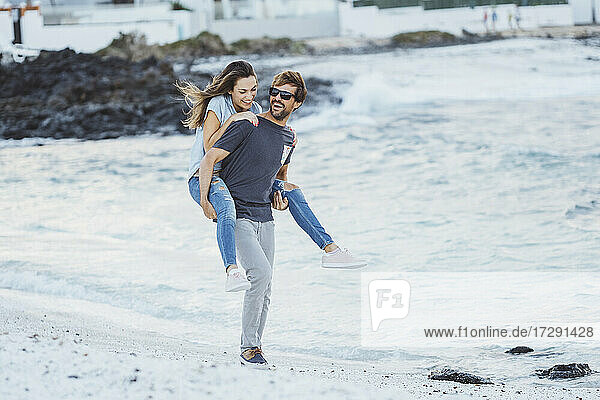 Cheerful girlfriend enjoying while piggybacking on boyfriend at beach