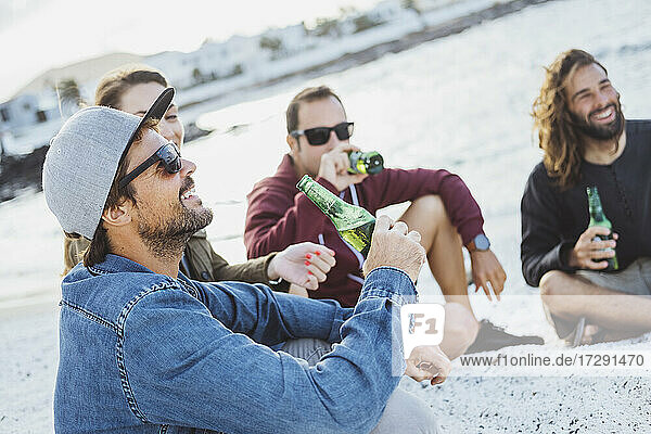 Lächelnder Mann mit Getränk  der mit Freunden am Strand sitzt