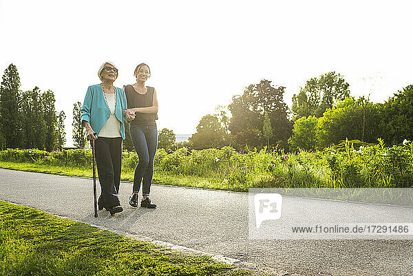 Mittlere erwachsene Frau  die eine ältere Frau beim Spazierengehen im Park stützt