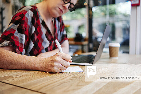 Frau schreibt auf Papier am Tisch im Café