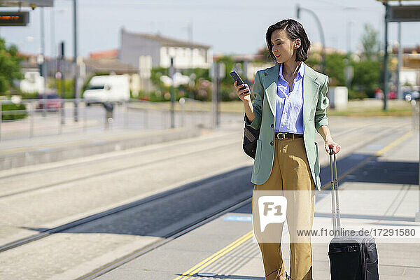 Weibliche Fachkraft  die ihr Smartphone benutzt  während sie am Bahnhof auf einen Zug wartet