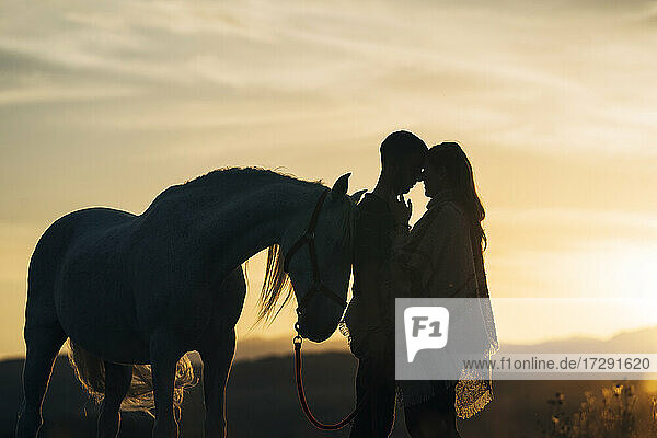 Romantisches junges Paar mit Pferd bei Sonnenuntergang