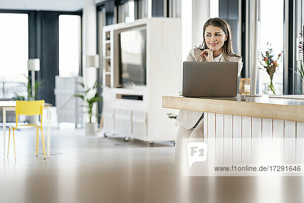 Lächelnde Geschäftsfrau  die in einer Cafeteria vor einem Laptop steht und nachdenkt