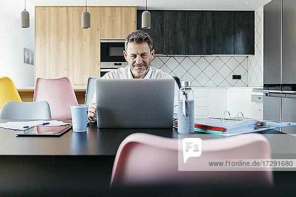Lächelnde männliche Fachkraft  die im Heimbüro auf einen Laptop schaut