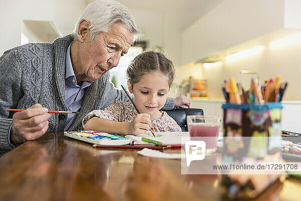 Granddaughter and grandfather painting together at home