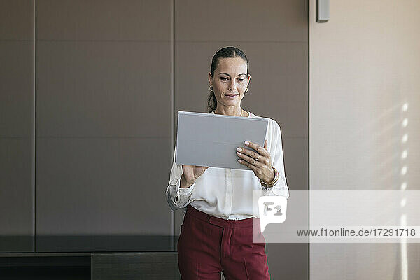 Reife Geschäftsfrau  die im Stehen im Büro ein digitales Tablet benutzt