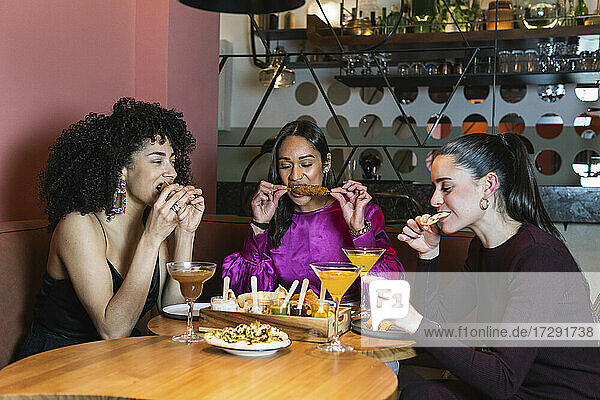 Young friends eating food while sitting in restaurant