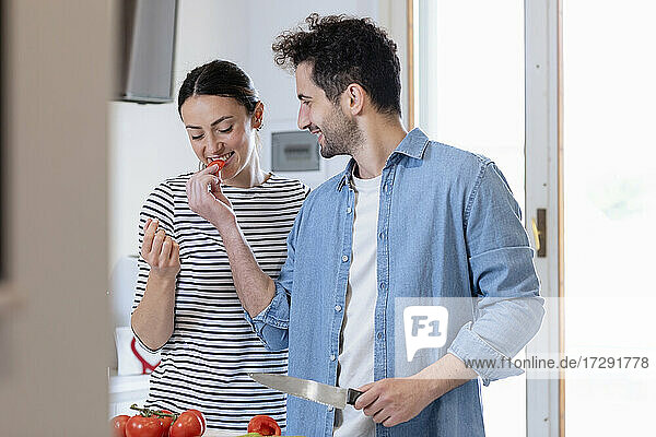 Lächelnder Freund füttert seine Freundin in der Küche zu Hause mit Tomaten