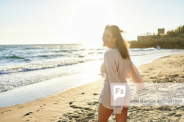 Lächelnde Frau schaut beim Strandspaziergang über die Schulter