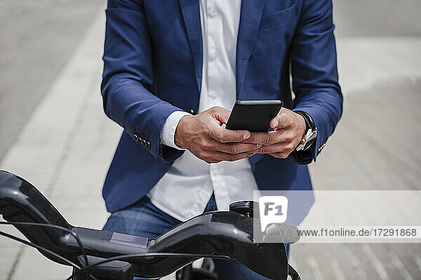 Businessman with rented electric bicycle using mobile phone on footpath