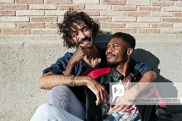 Smiling gay couple sitting in front of brick wall