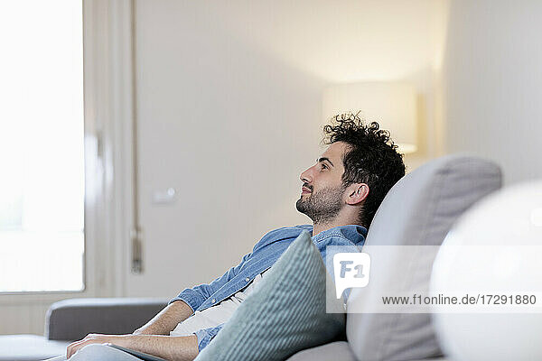 Mid adult man day dreaming while sitting on sofa in living room