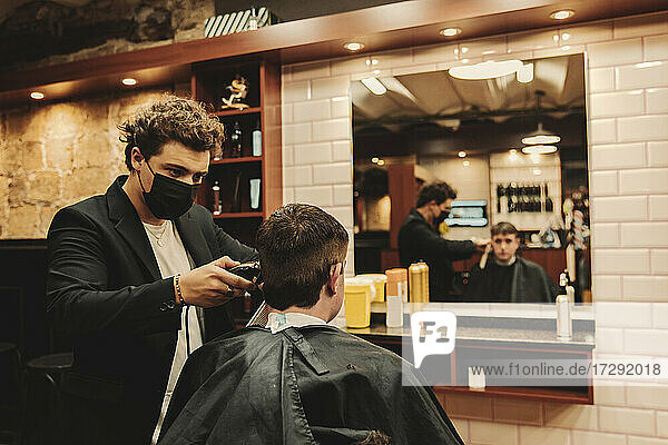 Männlicher Friseur beim Schneiden der Haare eines Kunden in einem Salon während einer Pandemie