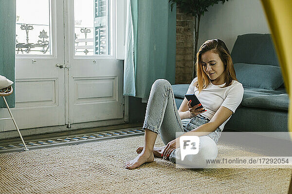 Relaxed woman using mobile phone while sitting on carpet at home