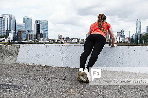 Female athlete doing warm up exercise over retaining wall in city