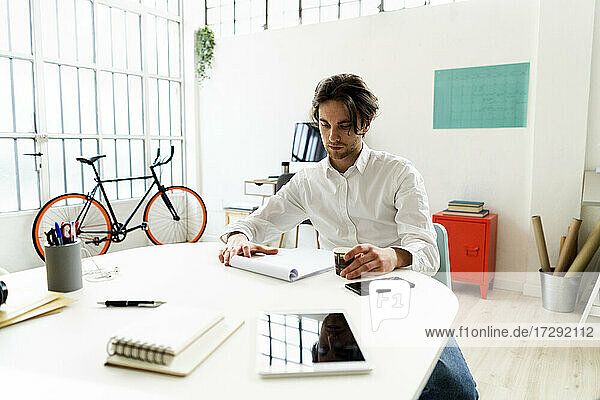 Männlicher Unternehmer  der einen Notizblock überprüft  während er in einem kreativen Büro sitzt