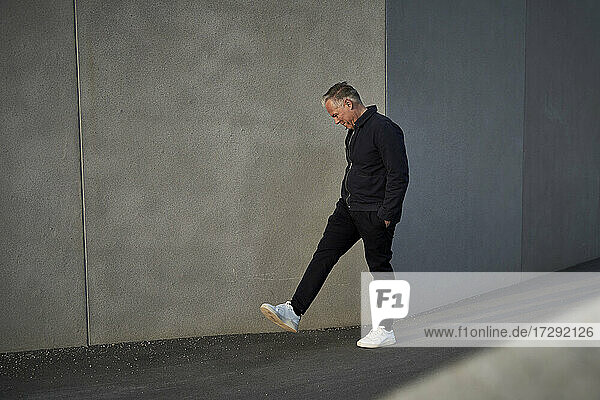 Businessman with hands in pockets walking by wall