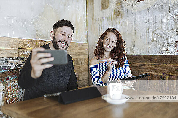 Mann macht Selfie mit einer Kollegin  die ein Grafiktablett in einem Café hält