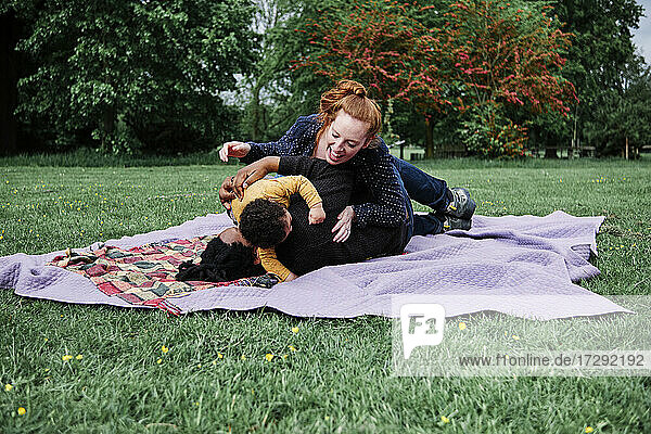 Eltern spielen mit ihrem Sohn auf einer Picknickdecke im Park