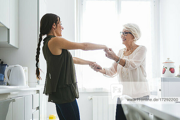 Großmutter und Enkelin halten sich an den Händen und tanzen zusammen in der Küche zu Hause
