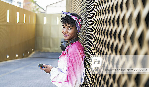 Schöne junge Frau mit Kopfhörern  die ihr Mobiltelefon an der Wand hält