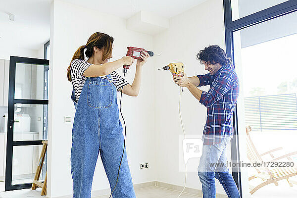 Mid adult couple playing with drill machine in new home