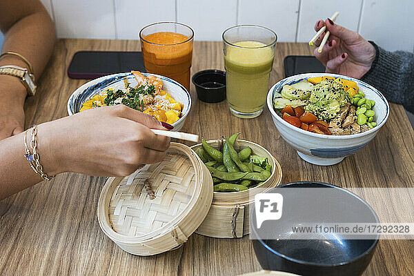 Female friends eating Chinese food with edamame beans in basket at restaurant