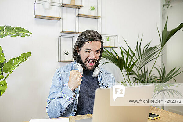 Männlicher Profi gestikuliert mit der Faust während eines Videoanrufs über einen Laptop im Büro